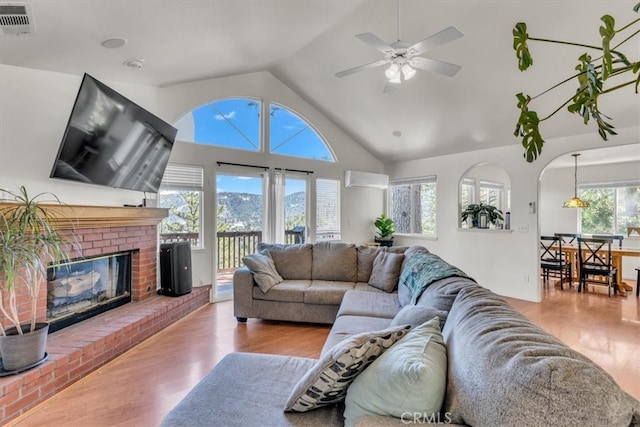 living room featuring visible vents, a brick fireplace, a wall mounted air conditioner, and wood finished floors