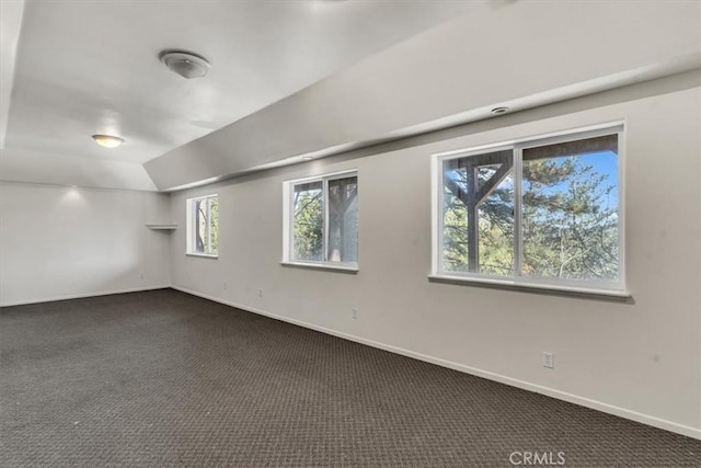 empty room featuring lofted ceiling, baseboards, and dark colored carpet