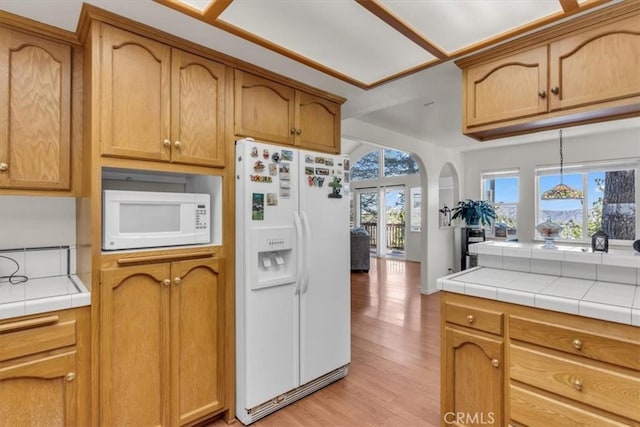 kitchen featuring arched walkways, tile countertops, white appliances, and light wood-type flooring