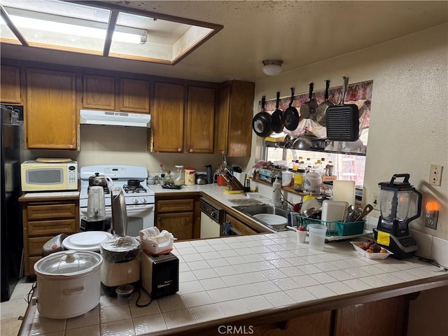 kitchen with under cabinet range hood, white appliances, tile countertops, and a sink