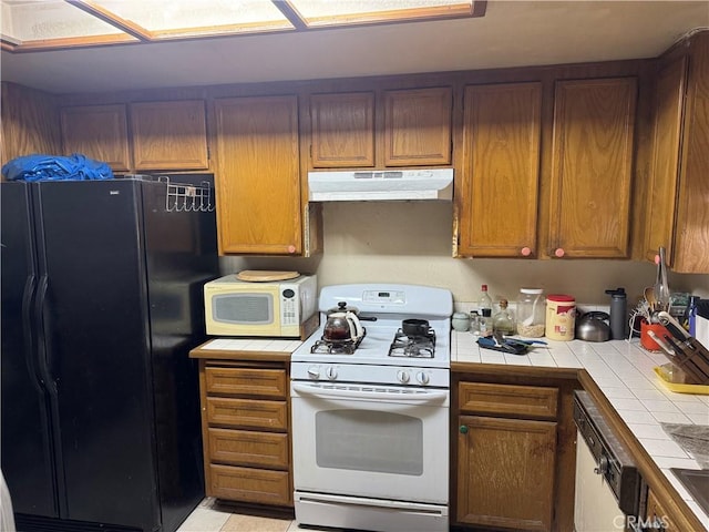 kitchen with white appliances, tile countertops, brown cabinets, and under cabinet range hood