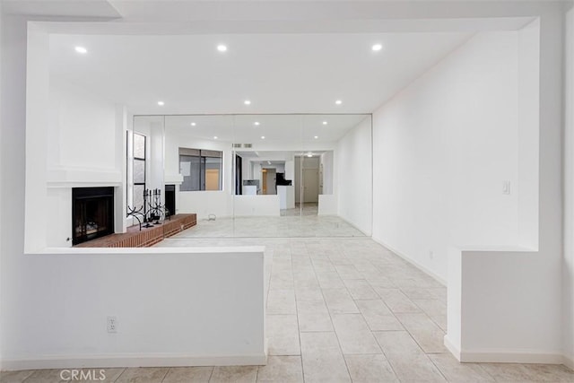 unfurnished living room with recessed lighting, a fireplace with raised hearth, and baseboards