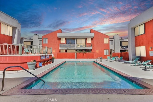 pool at dusk with a patio, a community pool, and fence