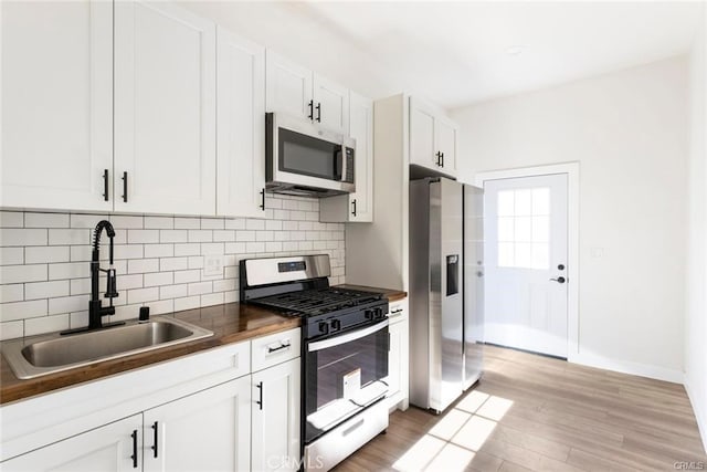 kitchen featuring a sink, tasteful backsplash, stainless steel appliances, white cabinets, and light wood finished floors