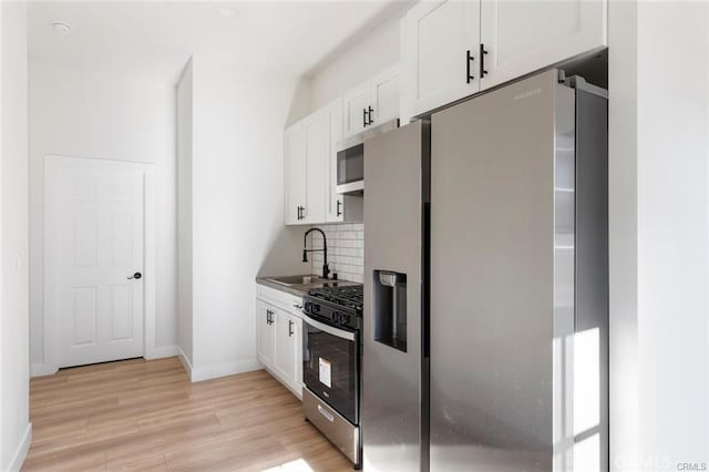 kitchen featuring light wood-type flooring, a sink, backsplash, white cabinetry, and stainless steel appliances