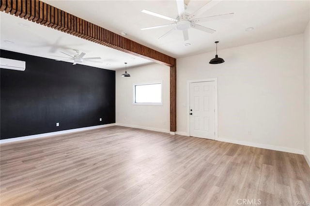 unfurnished room featuring light wood finished floors, baseboards, a wall mounted AC, and ceiling fan