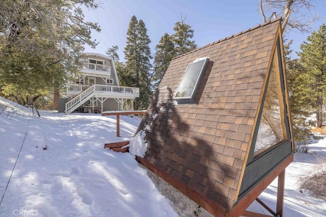 snow covered property with a balcony, stairs, and a shingled roof