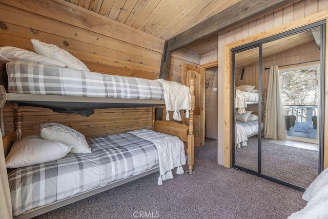 bedroom with wooden ceiling, carpet, a closet, and wood walls