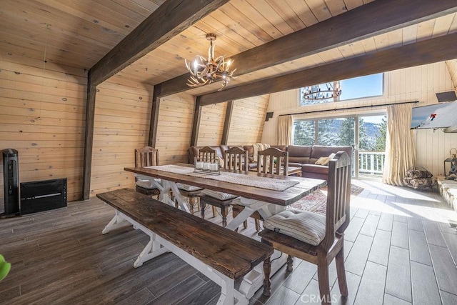 dining room with beam ceiling, wood walls, an inviting chandelier, and wood finished floors