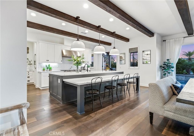 kitchen featuring dark wood finished floors, a breakfast bar, decorative backsplash, a large island with sink, and white cabinetry