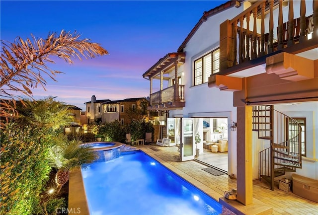 pool at dusk with stairway, a patio area, and a pool with connected hot tub