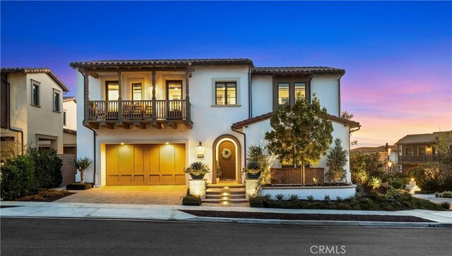 mediterranean / spanish-style house with a tiled roof, stucco siding, decorative driveway, a garage, and a balcony