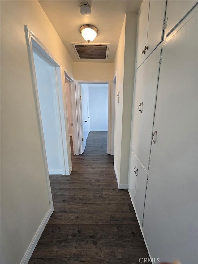 hallway featuring dark wood finished floors, visible vents, and baseboards