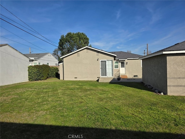 rear view of house with entry steps, crawl space, a lawn, and stucco siding