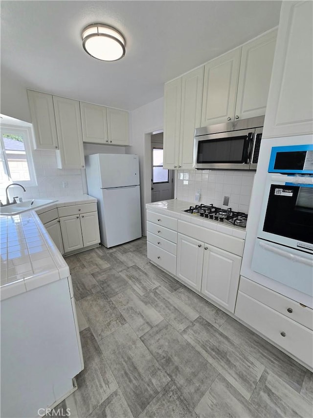 kitchen featuring a wealth of natural light, a sink, appliances with stainless steel finishes, white cabinets, and tile counters