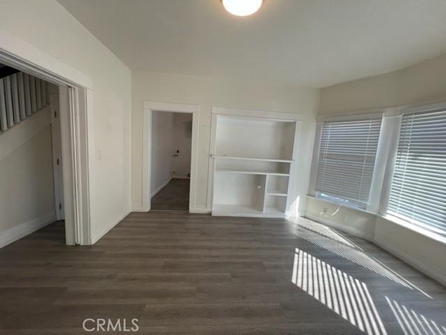 spare room with built in shelves, baseboards, and wood finished floors