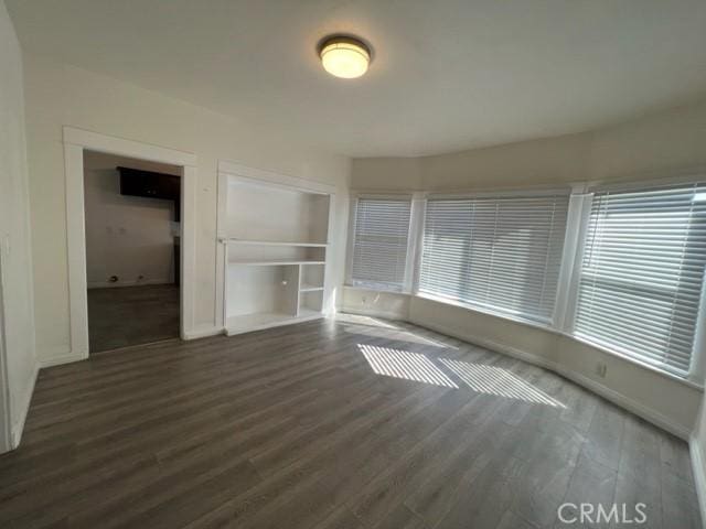 empty room featuring built in features, wood finished floors, and baseboards