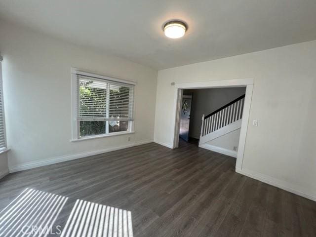 spare room featuring stairway, dark wood-style floors, and baseboards