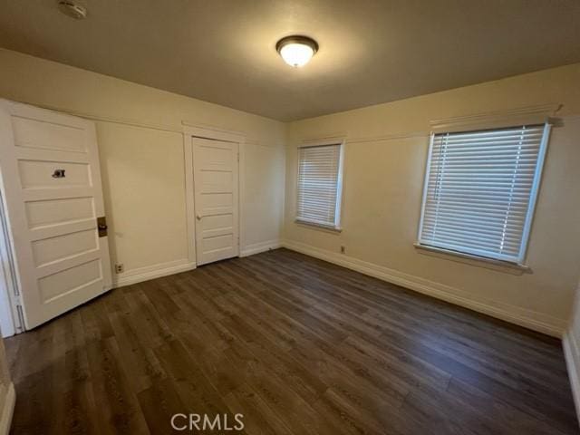 unfurnished bedroom featuring dark wood-type flooring, baseboards, and a closet