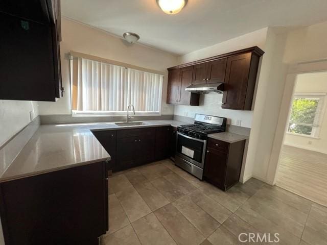 kitchen featuring dark brown cabinets, under cabinet range hood, light countertops, gas stove, and a sink