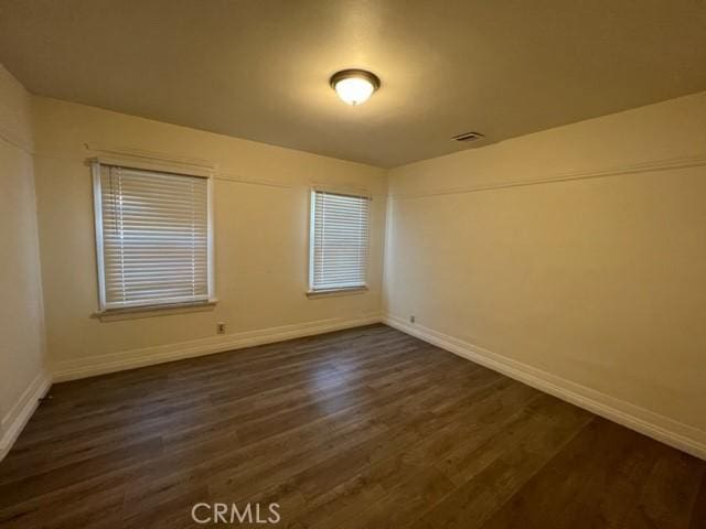 unfurnished room featuring visible vents, dark wood-style floors, and baseboards