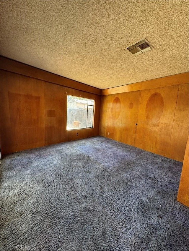 carpeted empty room with visible vents, a textured ceiling, and wooden walls