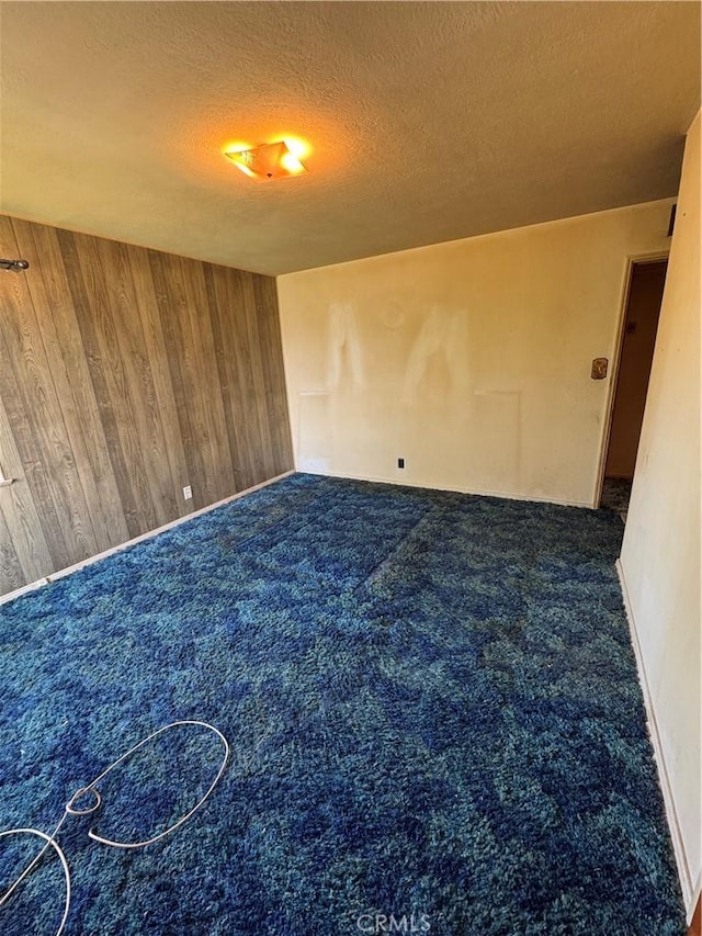 carpeted spare room featuring wooden walls and a textured ceiling