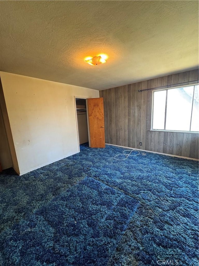 unfurnished bedroom with dark colored carpet, a closet, a textured ceiling, and wood walls