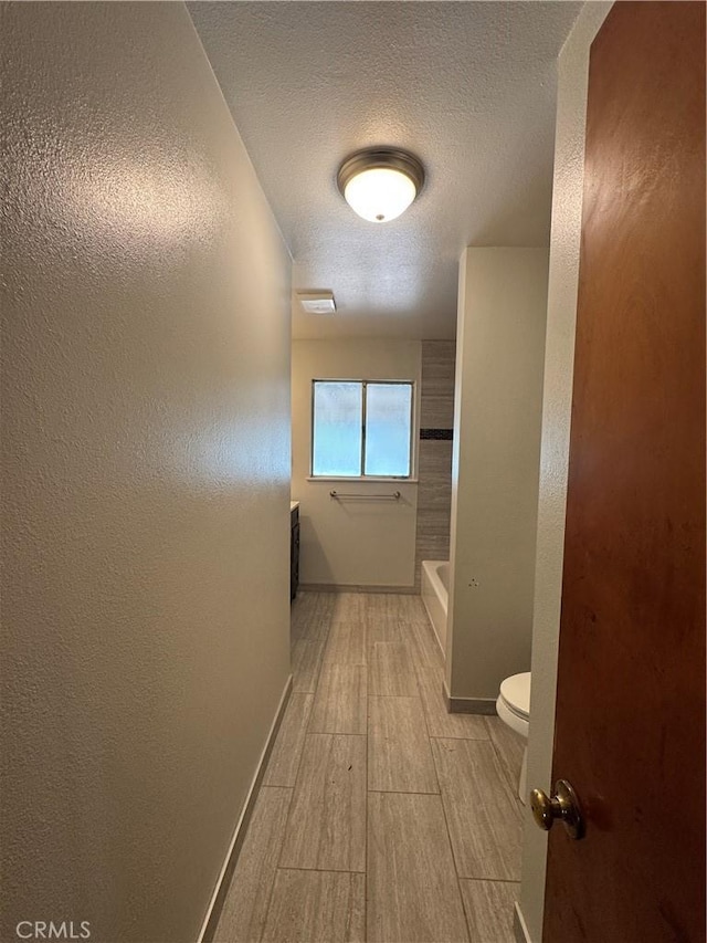 hall with wood tiled floor, a textured wall, baseboards, and a textured ceiling