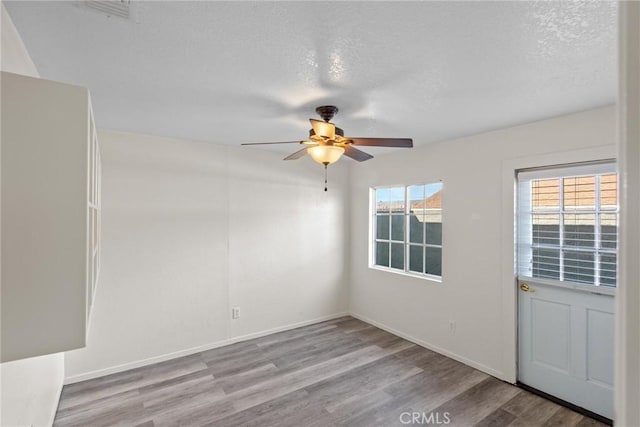 empty room featuring ceiling fan, wood finished floors, baseboards, and a textured ceiling