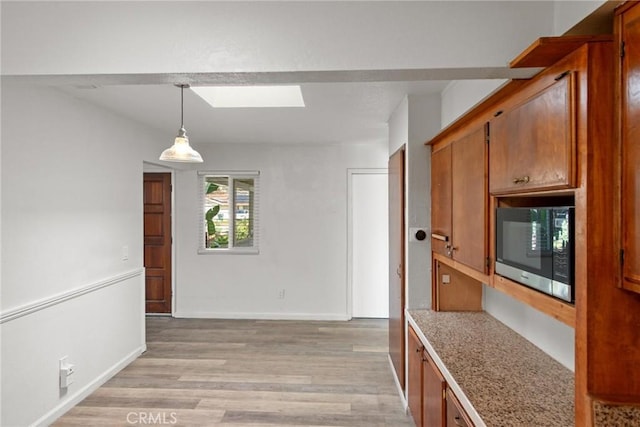 kitchen featuring stainless steel microwave, light wood-type flooring, light countertops, brown cabinets, and a skylight