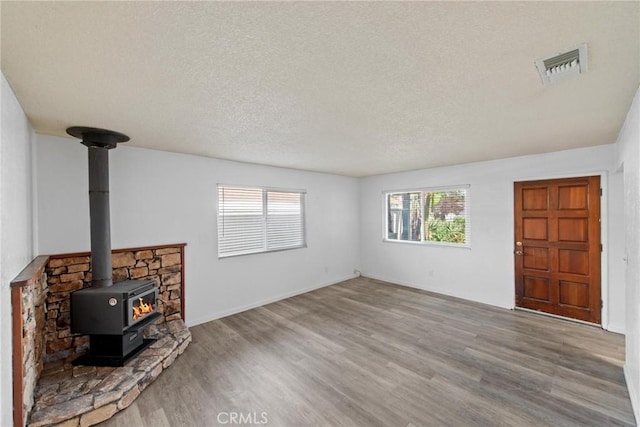 unfurnished living room with visible vents, a textured ceiling, wood finished floors, and a wood stove