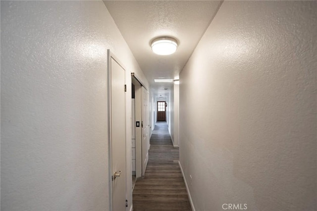 hall featuring a textured ceiling, wood finished floors, baseboards, and a textured wall