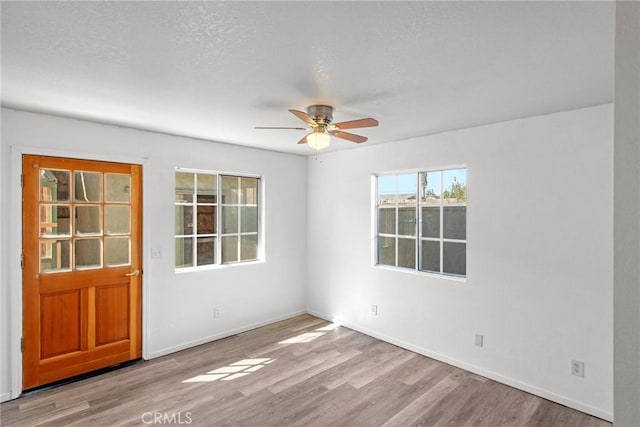 unfurnished room with a textured ceiling, wood finished floors, baseboards, and ceiling fan