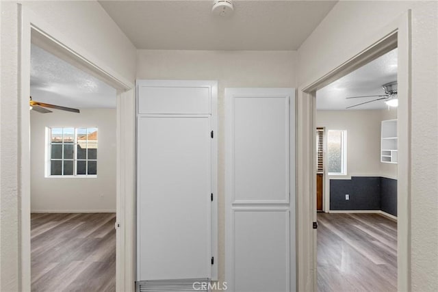 corridor with baseboards, a textured ceiling, and wood finished floors