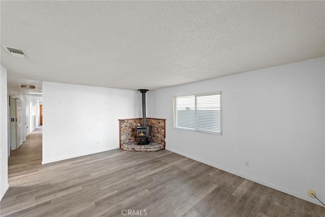 unfurnished living room featuring a wood stove, wood finished floors, visible vents, and a textured ceiling