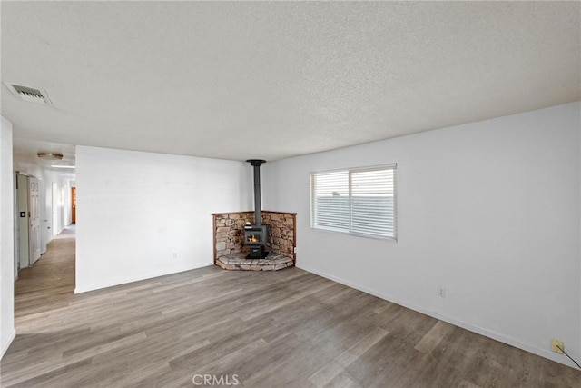 1429 14th St, Los Osos, CA 93402 - unfurnished living room with visible vents, baseboards, a wood stove, a textured ceiling, and wood finished floors