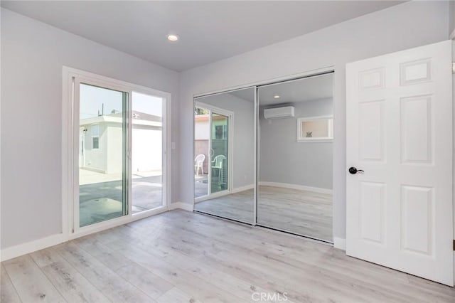 unfurnished bedroom featuring access to exterior, light wood-style floors, baseboards, and a wall mounted air conditioner