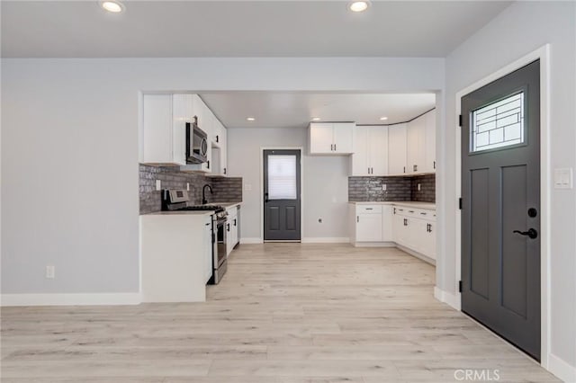 kitchen featuring light wood finished floors, white cabinets, stainless steel appliances, and baseboards