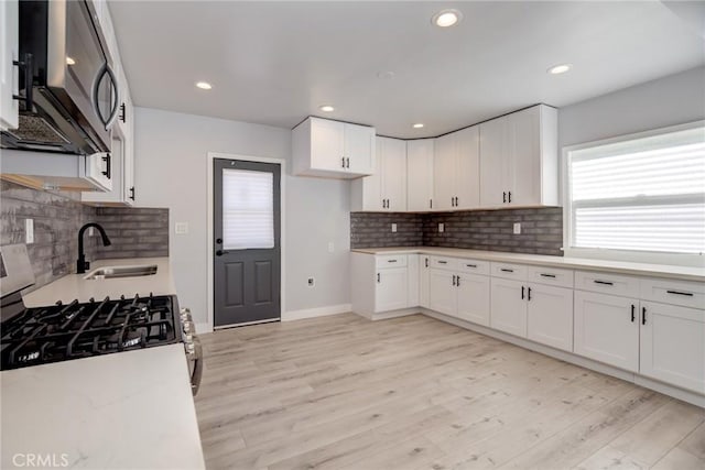 kitchen featuring white cabinetry, stainless steel microwave, light wood-style flooring, and a sink