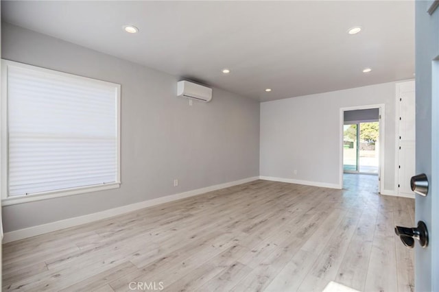 empty room featuring recessed lighting, light wood-type flooring, a wall mounted air conditioner, and baseboards