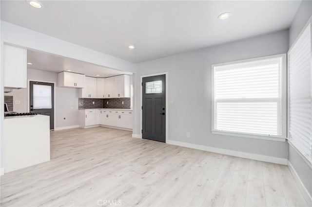 kitchen featuring light wood finished floors, decorative backsplash, white cabinets, and baseboards