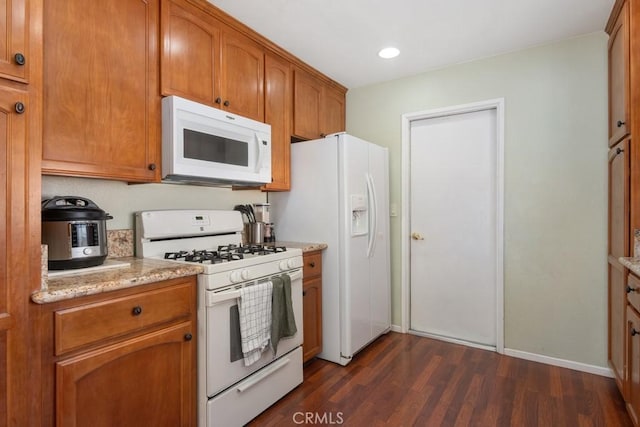 kitchen with brown cabinets, light stone counters, white appliances, baseboards, and dark wood-style flooring