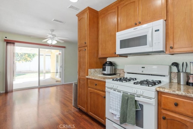 kitchen featuring light stone counters, visible vents, white appliances, and dark wood-style flooring