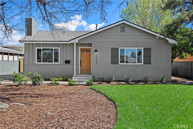 view of front of house with board and batten siding, a front lawn, fence, entry steps, and a chimney