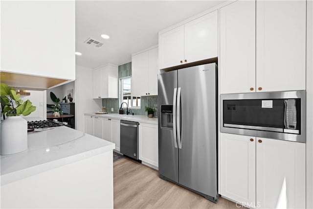 kitchen featuring visible vents, light wood-type flooring, light stone counters, appliances with stainless steel finishes, and white cabinets