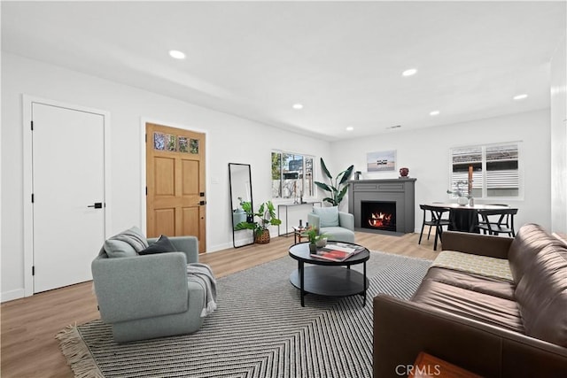 living area featuring a fireplace with flush hearth, recessed lighting, baseboards, and light wood finished floors