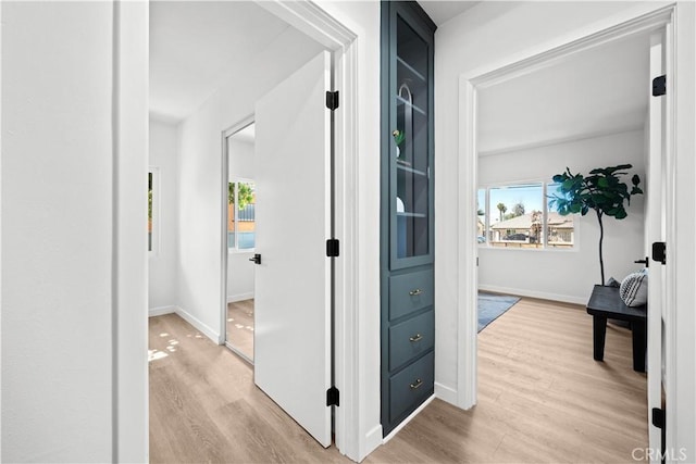 hallway featuring light wood finished floors and baseboards