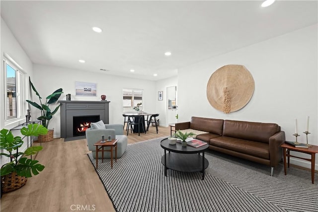 living area featuring recessed lighting, baseboards, a brick fireplace, and light wood finished floors