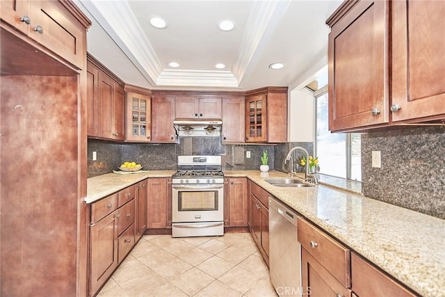 kitchen with a raised ceiling, light stone countertops, appliances with stainless steel finishes, and a sink